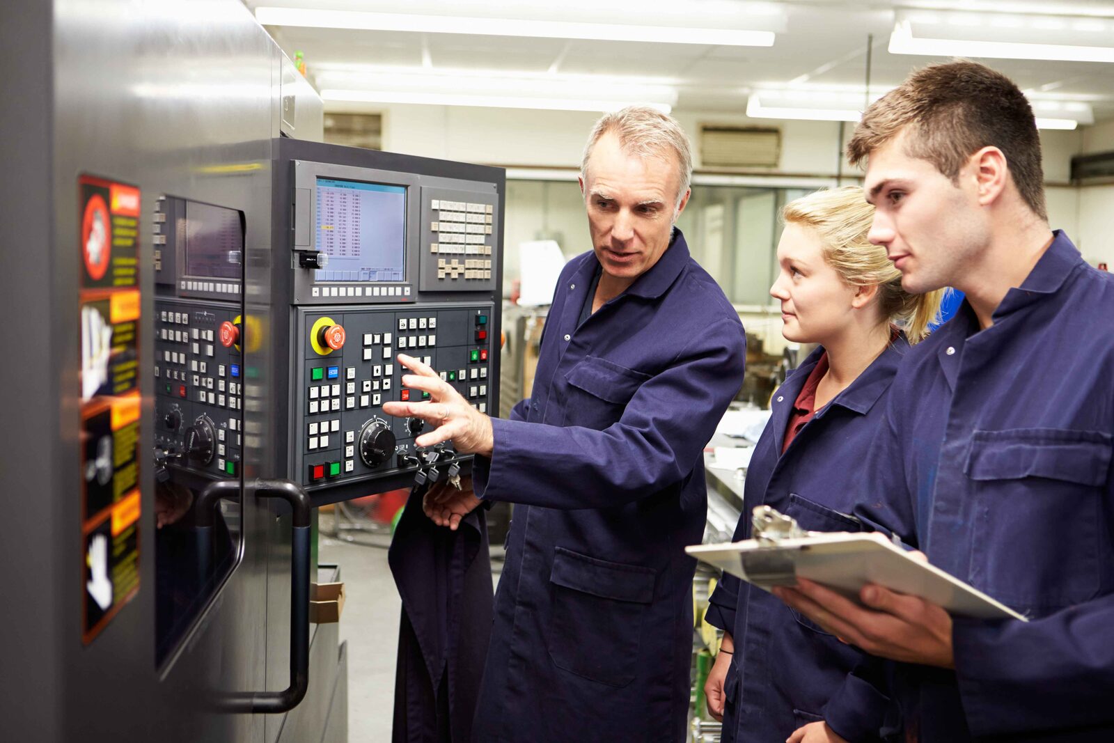Three factory workers inspect a control panel on industrial machinery during a vet compliance assessment.