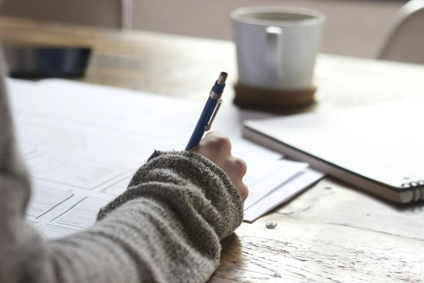A person writes on paper with a pen while enjoying coffee, illustrating vocational education training.