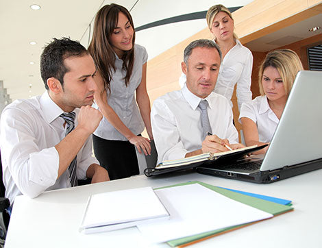 A business team collaborates around a laptop during an office meeting, demonstrating effective vet compliance.